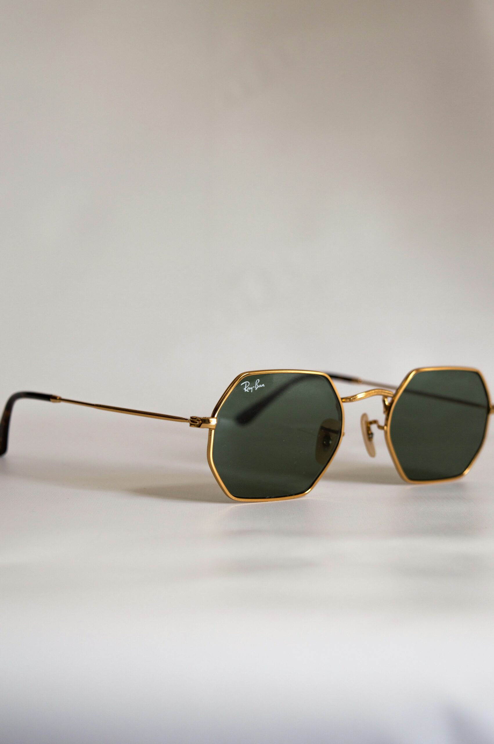 A pair of gold-framed hexagonal sunglasses with dark green lenses placed on a light surface.